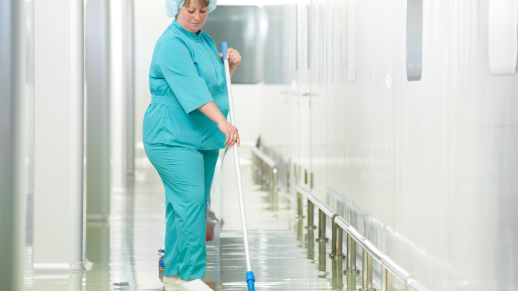 agent de bionettoyage passant le balai de lavage à plat dans un couloir d'hôpital